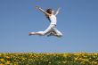 Girl flying in a jump over dandelion field