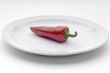 Single red chile pepper on a white plate