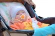 Little girl with baby`s dummy sit in carriage.