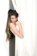 Beautiful young woman looking from behind a white curtain