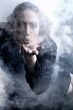 Woman with long curly hair blowing smoke