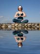 A woman doing yoga on a stone above  water