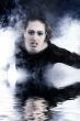 Woman with long curly hair crawling out of smoke