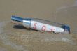 Message in a bottle with SOS signal lying in surf