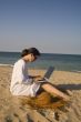 Woman sitting on beach with laptop