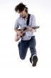young male jumping high holding his guitar