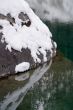 Big stone covered a snow in nonfreezing blue lake.