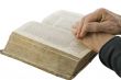 Male hands closed in prayer on an open bible isolated over white