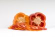 Cut orange and red sweet pepper showing seeds with slices on whi