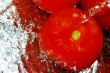 Fresh tomatoes under running tap with water drops