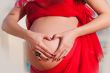 Pregnant woman in red with hand heart.