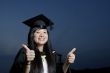 Smiling asian female graduate with thumbs up sign