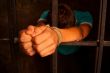 Man with hands tied with rope behind the bars