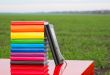 Stack of colorful books and electronic book reader outdoors
