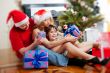 Young happy family near a Christmas tree at home holding gifts.