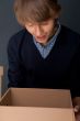 Portrait of young man holding on box against grey wall. 