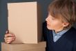 Portrait of young man holding on box against grey wall.