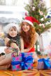 Little girl with her mother sitting together near christmas tree