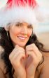 Young beautiful woman wearing christmas hat showing heart shape 