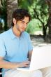 Portrait of a young man with laptop outdoor sitting on bench