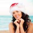 Young beautiful woman wearing christmas hat showing heart shape 