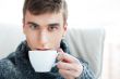 Portrait of a young man drinking coffee while sitting on armchai