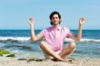 Portrait of young man sitting in lotus pose on sand on beach and