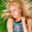 Young woman laying on green grass with hair like a sun around he