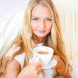 Smiling woman drinking a coffee lying on a bed at home or hotel.