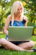 Beautiful student woman with a laptop sitting on green grass at 