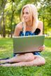 Beautiful student woman with a laptop sitting on green grass at 