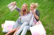 Portrait of two women relaxing on green grass after shopping. Ho