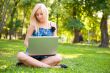 Beautiful student woman with a laptop sitting on green grass at 