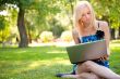Beautiful student woman with a laptop sitting on green grass at 