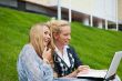 Portrait of two smiling women using laptop on a green meadow at 