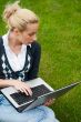 Young woman with laptop sitting on green grass and looking to th