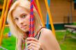 Portrait of pretty young woman swinging on playground at park an