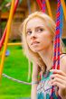 Portrait of pretty young woman swinging on playground at park an