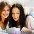 Two excited shopping woman resting on bench at shopping mall loo