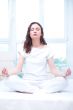Young woman meditating with closed eyes in bright bedroom sittin