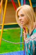 Portrait of pretty young woman swinging on playground at park an