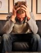 Closeup portrait of young man sitting on sofa with headache