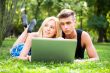Portrait of young couple outdoor resting on green grass and usin