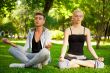 Portrait of young beautiful couple sitting in lotus pose on gree