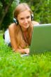 A smiling young girl with laptop outdoors listening music by hea