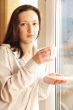 Portrait of cosy young girl standing near a window at home