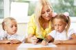 Teacher helps to little girls to make an exercises in classroom