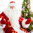 Santa sitting at the Christmas tree, near fireplace and looking 