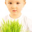 Happy little boy holding green grass in his arms and looking ser
