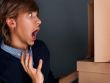 Portrait of young man with boxes against grey wall. He is afraid